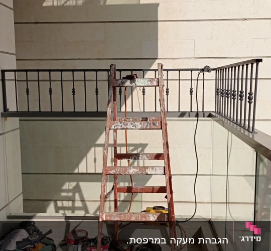 סולם עץ מול מעקה מתכת עם כלים על הרצפה